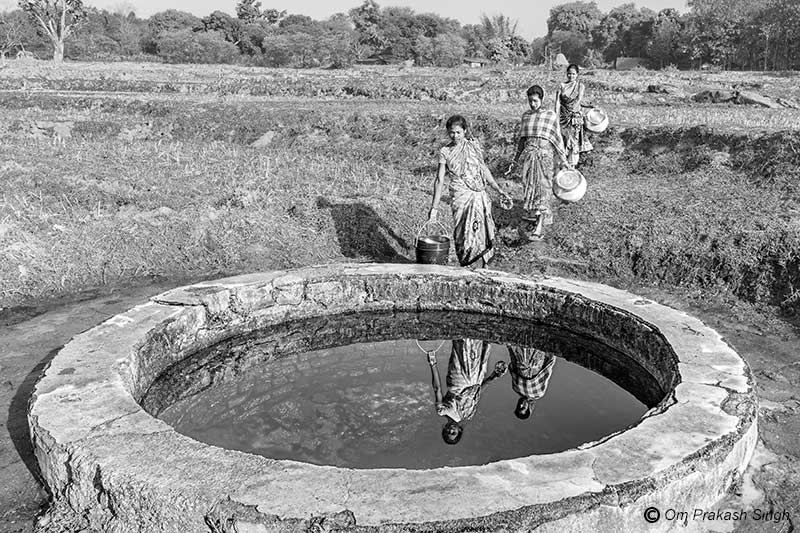 Preparing to collect drinking water from a spring-based traditional source located amidst distant paddy fields in Khunti district, Jharkhand, India